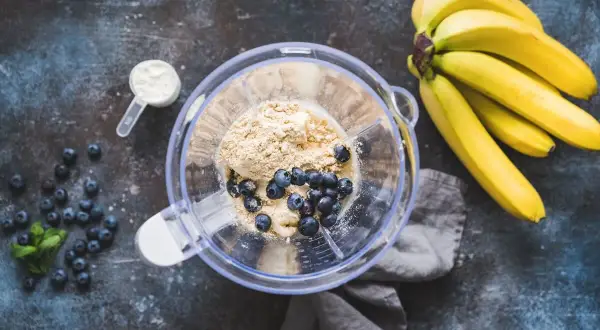 Składniki na pyszny shake proteinowy: banany, borówki, odżywka białkowa w proszku i miętka.