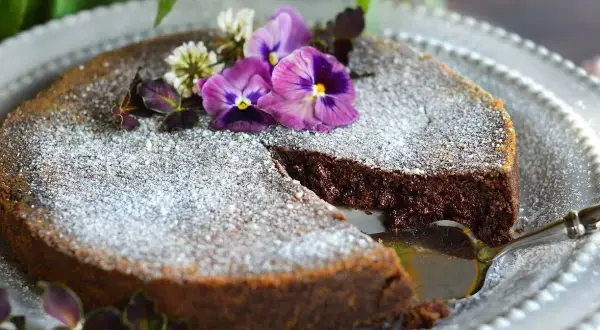 En saftig tårta med chokladpudding, pudrad med florsocker och dekorerad med violer och klöver. En bit är uppskuren.