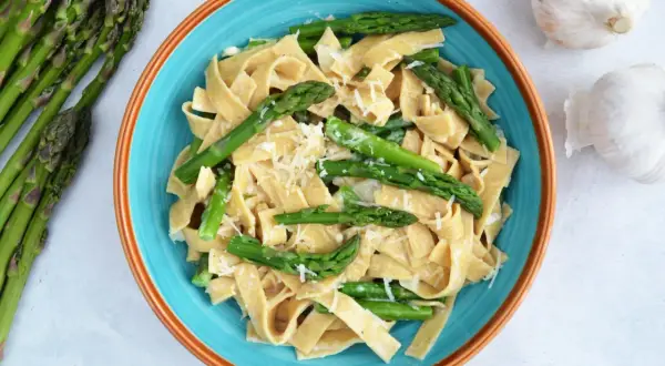 Makaron tagliatelle z zielonymi szparagami i startym parmezanem w niebieskiej misce.