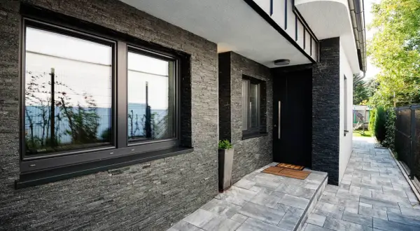 Nowoczesny dom z kamienną elewacją i czarnymi oknami. Świetny pomysł na elewację domu, który nadaje mu elegancki i minimalistyczny charakter.