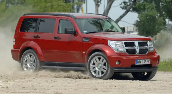 Czerwony Dodge Nitro z impetem wjeżdża na piaszczystą drogę, wzbijając tumany kurzu.