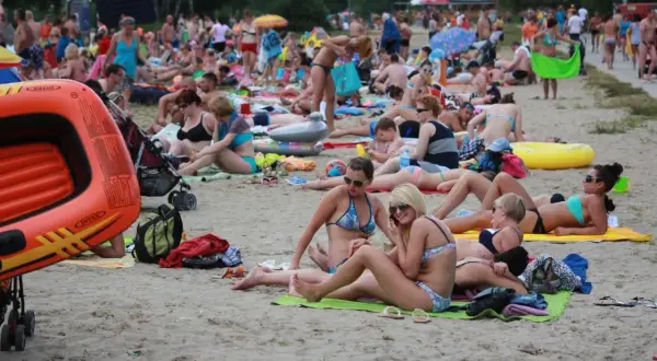 Tłum ludzi odpoczywa na plaży nad jednym z lubelskich jezior. Wszyscy w strojach kąpielowych, opalają się i relaksują.