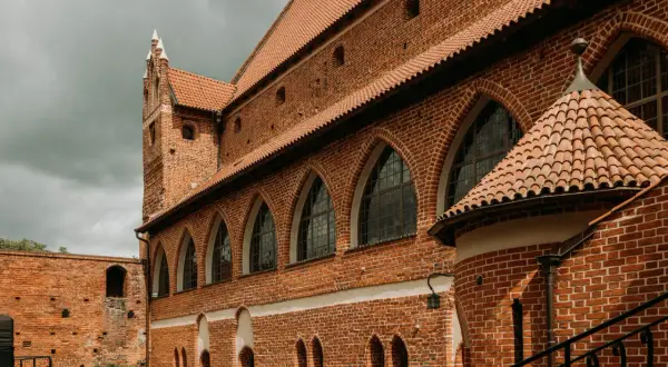 Zamek kapituły warmińskiej w Fromborku, z ceglanymi murami, arkadowymi oknami i charakterystycznym dachem.