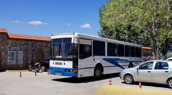 Biały autobus z niebieskimi pasami, oznaczony jako "Arbus", stoi zaparkowany obok kamiennego muru. To autobus z Macedonii, gotowy na kolejną podróż.