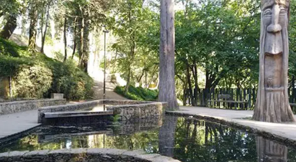 Escultura de madera en el parque de los sentidos, junto a estanques de agua y vegetación exuberante.