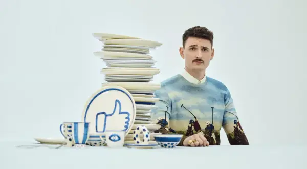 Mężczyzna z wąsikiem w swetrze z motywem polo, obok stosu talerzy i zastawy z symbolem "like". Stylizacja jak z lat dwudziestych.