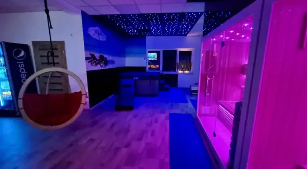 Nowoczesne spa z sauną, jacuzzi i wiszącym fotelem, oświetlone neonowym światłem.