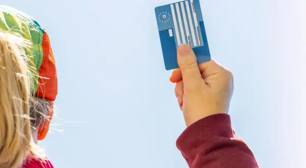 Karta EKUZ dla dziecka – jak wyrobić? Ręka trzyma niebieską kartę EKUZ na tle błękitnego nieba.