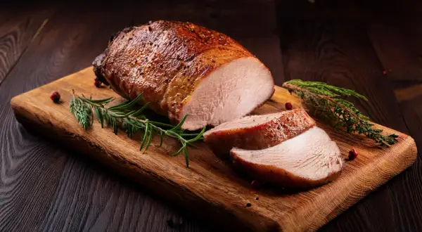 Saftiges Schweinefilet, angebraten und dann im Ofen perfekt gegart, liegt auf einem Holzbrett, garniert mit Rosmarin und Pfefferkörnern.