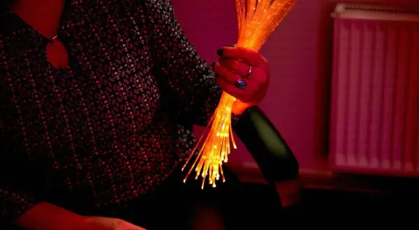 Une main tient un bouquet de fibres optiques lumineuses, évoquant l'univers apaisant du snoezelen.