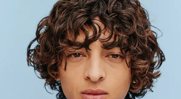 Gros plan sur le visage d'un homme aux cheveux bruns ondulés, type cheveux 2b homme, sur fond bleu clair.