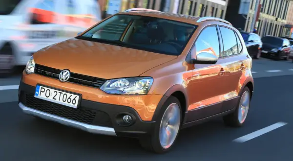 Pomarańczowy Volkswagen Polo Cross w ruchu miejskim, z widocznym kierowcą i innymi samochodami w tle.