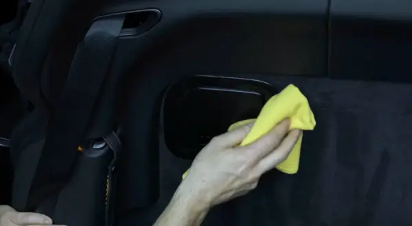 Hand reinigt mit gelbem Tuch den schwarzen Kunststoff im Auto.