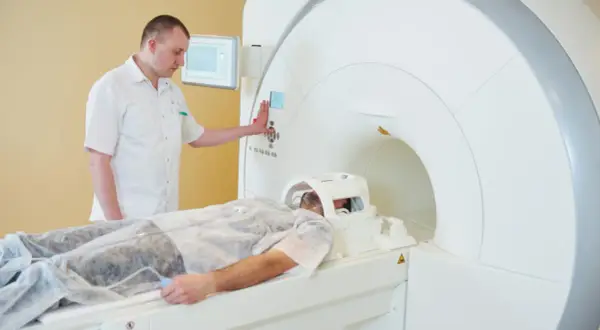 Pacjent leży w aparacie do rezonansu magnetycznego. Technik nadzoruje badanie, przygotowując rejestrację.