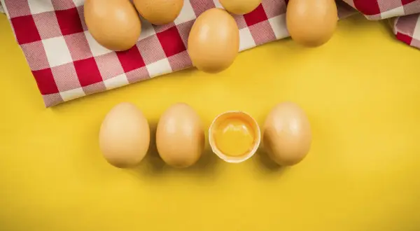 Uova su sfondo giallo, una rotta mostra il tuorlo. Quante uova si possono mangiare al giorno?