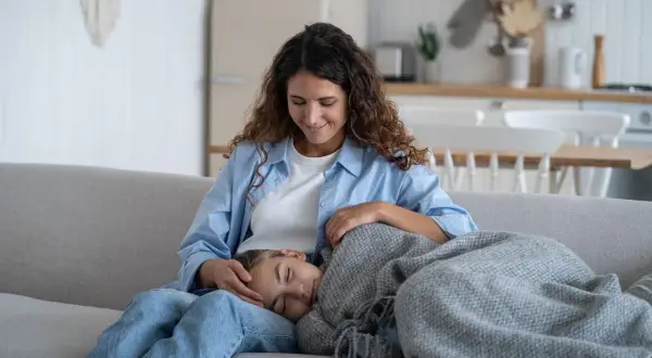 Madre reconforta a su hija, que duerme en su regazo. La menstruación a los 10 años es normal y la madre le ofrece apoyo.