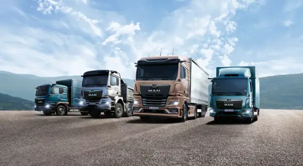 Quatre camions de la marque MAN, aux couleurs variées, roulent sur une route sous un ciel bleu nuageux.