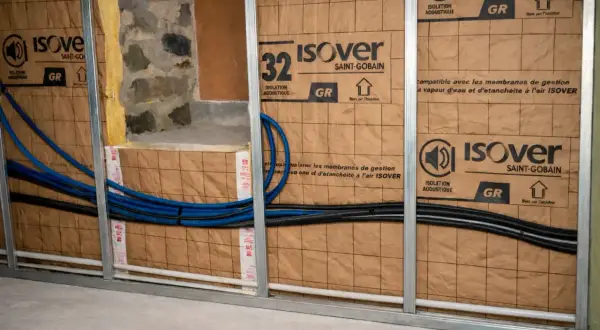 Pose rail placo pour isolation acoustique Isover. Tuyaux bleus et noirs passent derrière.