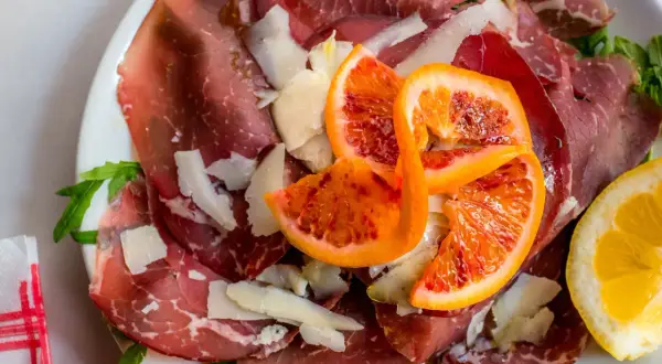 Bresaola co to? Delikatne plastry wędzonego mięsa wołowego, posypane parmezanem, z dodatkiem krwistych pomarańczy i cytryny.