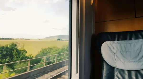 Blick aus dem Zugfenster auf grüne Felder während der zugreise nach wien. Ein bequemer Sitz im Vordergrund.