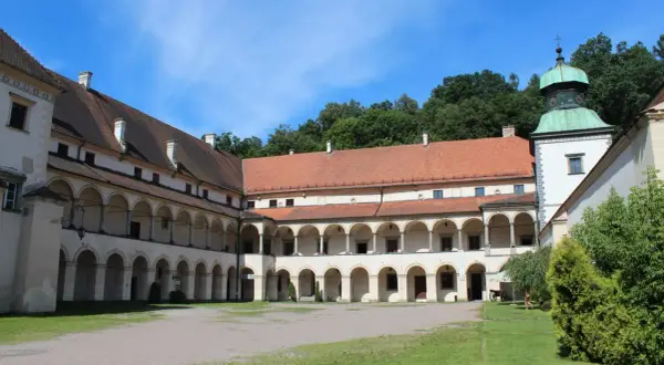 Dziedziniec zamku w Suchej Beskidzkiej z arkadowymi krużgankami i zieloną wieżą.