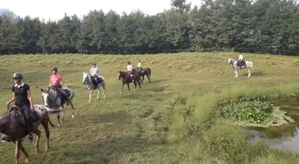 Cavalcata a Toscolano Maderno, un gruppo di persone a cavallo attraversa un prato verde vicino a un laghetto.