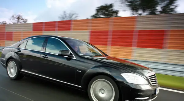 Czarny Mercedes S400d pędzi autostradą obok kolorowego ekranu dźwiękochłonnego.