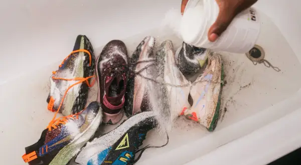 Mani versano polvere da un contenitore su diverse scarpe da ginnastica in una vasca da bagno, un modo per disinfettare scarpe usate.