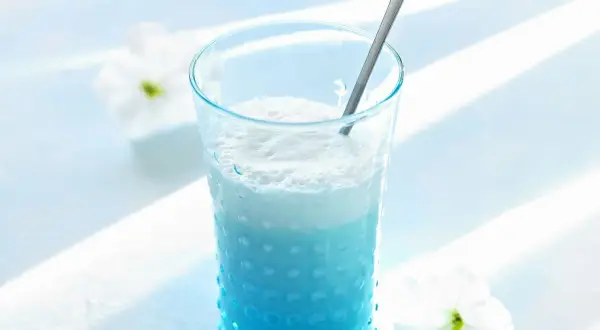 Ein erfrischender Blue Curacao Cocktail in einem strukturierten Glas, garniert mit weißen Blüten.
