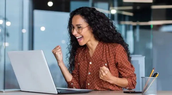 Excited woman celebrates fast Google Drive upload speed on her laptop.