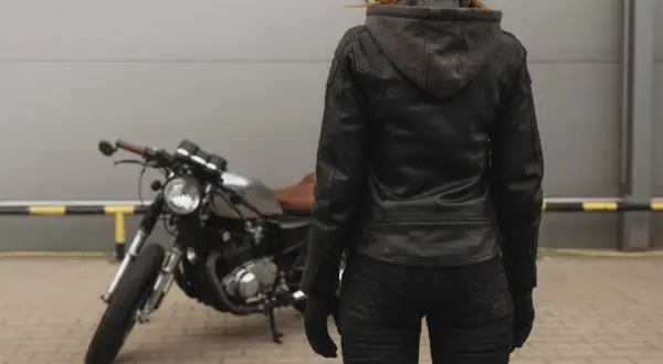 Kobieta w skórzanej kurtce motocyklowej i kasku stoi obok motocykla.