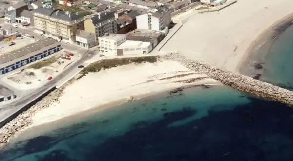 Vista aérea de la playa Penoural en Burela, con edificios urbanos y el mar azul turquesa.