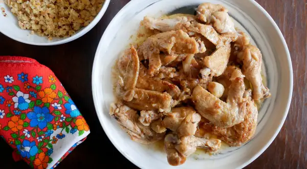 Alitas de pollo al ajillo, doradas y jugosas, servidas en un plato blanco. Acompañadas de quinoa y una servilleta colorida.
