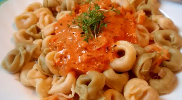 Kolorowe tortellini z kremowym sosem pomidorowym, udekorowane świeżymi ziołami. Pyszne danie gotowe do spożycia.