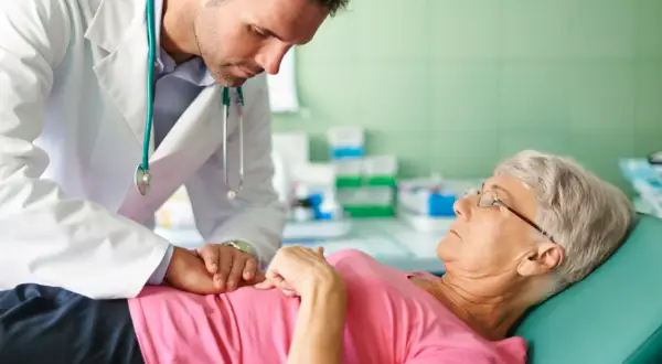 Lekarz w białym kitlu pochyla się nad pacjentką leżącą na kozetce.