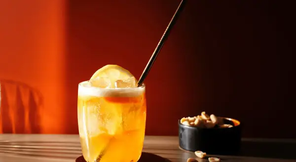 Ein erfrischender Amaretto Sour mit Zitrone und Eiswürfeln, daneben eine Schale Erdnüsse.