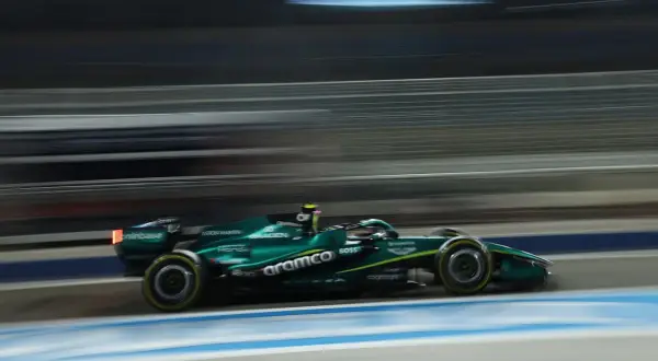 Un coche Aston Martin Honda verde compite a gran velocidad en una pista nocturna, con las luces y el fondo difuminados por el movimiento.