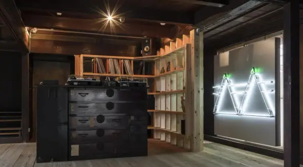 Theaster Gates studio: A DJ setup sits atop a dark wooden chest of drawers, surrounded by shelves of records and a striking neon art installation.