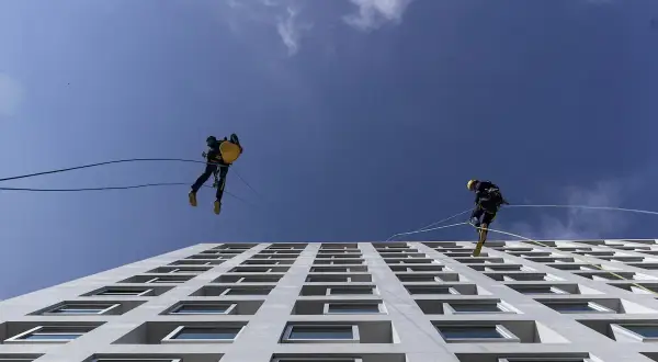 Lavoratori in corda assicurati da una linea vita tetto obbligatoria scendono lungo la facciata di un edificio moderno.