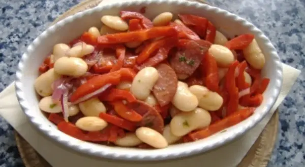 Ein herzhafter spanischer Bohnensalat mit weißen Bohnen, roten Paprikastreifen und Chorizo in einer weißen Schüssel.