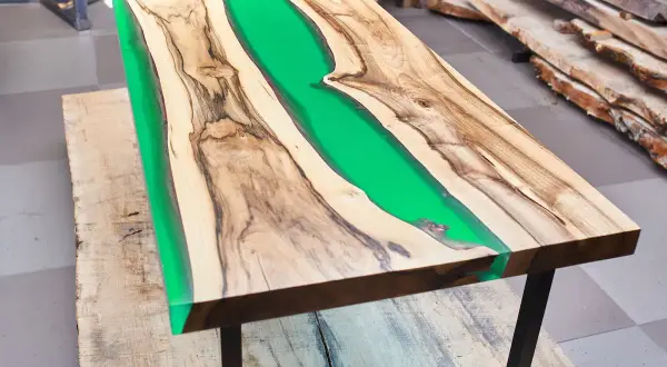 Tavolo con resina verde brillante tra venature di legno. La differenza tra levigatura e lucidatura è evidente nella finitura liscia e riflettente.