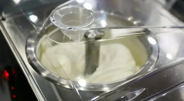 Cremiges Sahneeis wird in einer Eismaschine zubereitet. Der Rührarm dreht sich, um die perfekte Konsistenz zu erzeugen.
