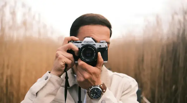 Man with a Canon AE-1, a classic choice for the best film camera for street photography, captures the moment amidst tall grasses.