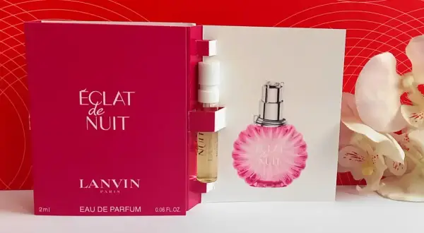 Próbka perfum Lanvin Éclat de Nuit, z buteleczką i kartonikiem z wizerunkiem flakonu, na tle czerwonych wzorów i białych kwiatów.