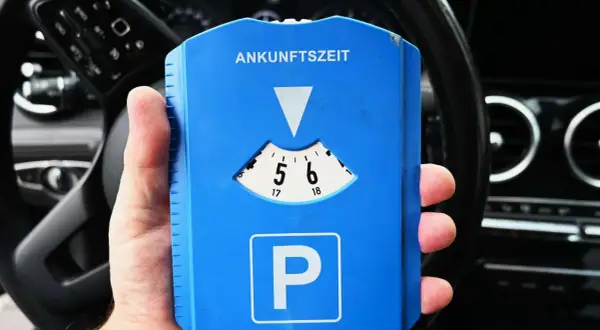 Blaue Parkscheibe mit "Ankunftszeit" und "P"-Symbol. Beachten Sie die Parkuhr Regeln für die korrekte Einstellung der Ankunftszeit.