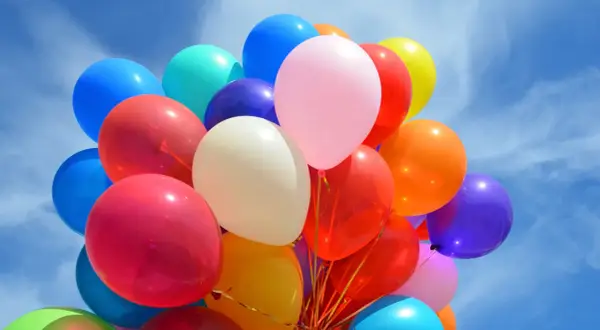 Kolorowe balony unoszą się na błękitnym niebie. Czy zwykłe balony można nadmuchać helem? Tak, jeśli są odpowiednio przygotowane.