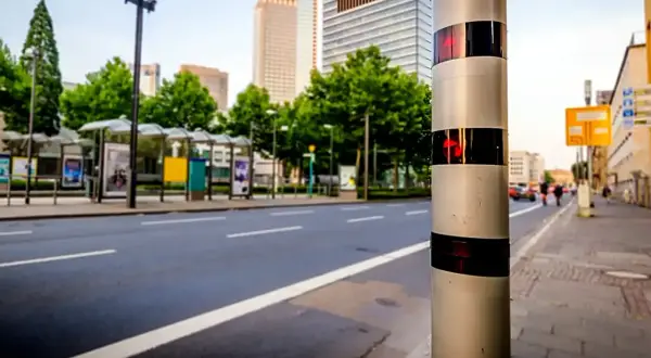 Blitzer am Straßenrand, bereit, Fahrer zu erwischen, die 31 kmh zu schnell auf der Autobahn fahren. Hohe Gebäude im Hintergrund.