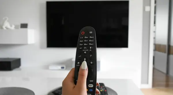 Dłoń trzymająca pilot do telewizora, gotowa do włączenia obrazu w rozdzielczości 4k.