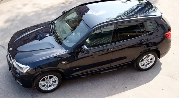 Ciemnogranatowe BMW X3, mocne auto tanie w utrzymaniu, lśni w słońcu. Widok z góry na błyszczący lakier i odbijające się budynki.