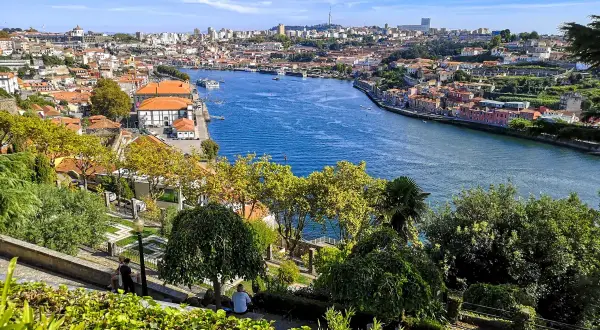 Widok na rzekę Douro i malownicze, kolorowe domy Porto. W oddali widać panoramę miasta, a na pierwszym planie zielony park.